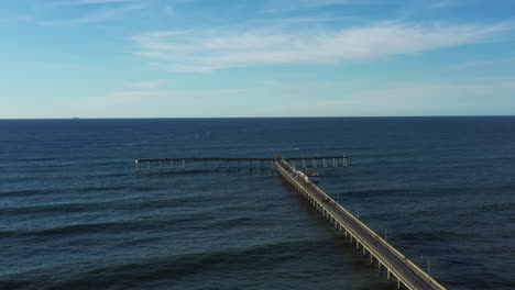 aerial flight over a pier leading out into the ocean and blue sky