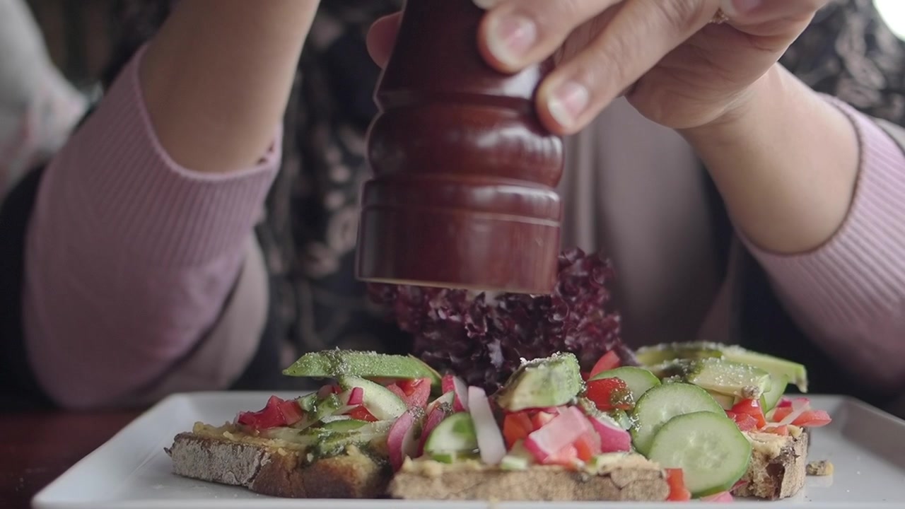 Person Seasoning Fresh Avocado Toast with Pepper Mill