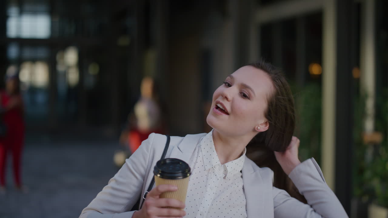 retrato joven feliz mujer de negocios riendo arreglando el cabello disfrutando de un estilo de vida relajado sosteniendo café en el aire libre urbano fondo cámara lenta