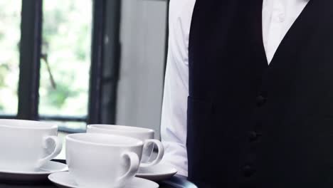 mid section of waiter holding a tray of coffee cups