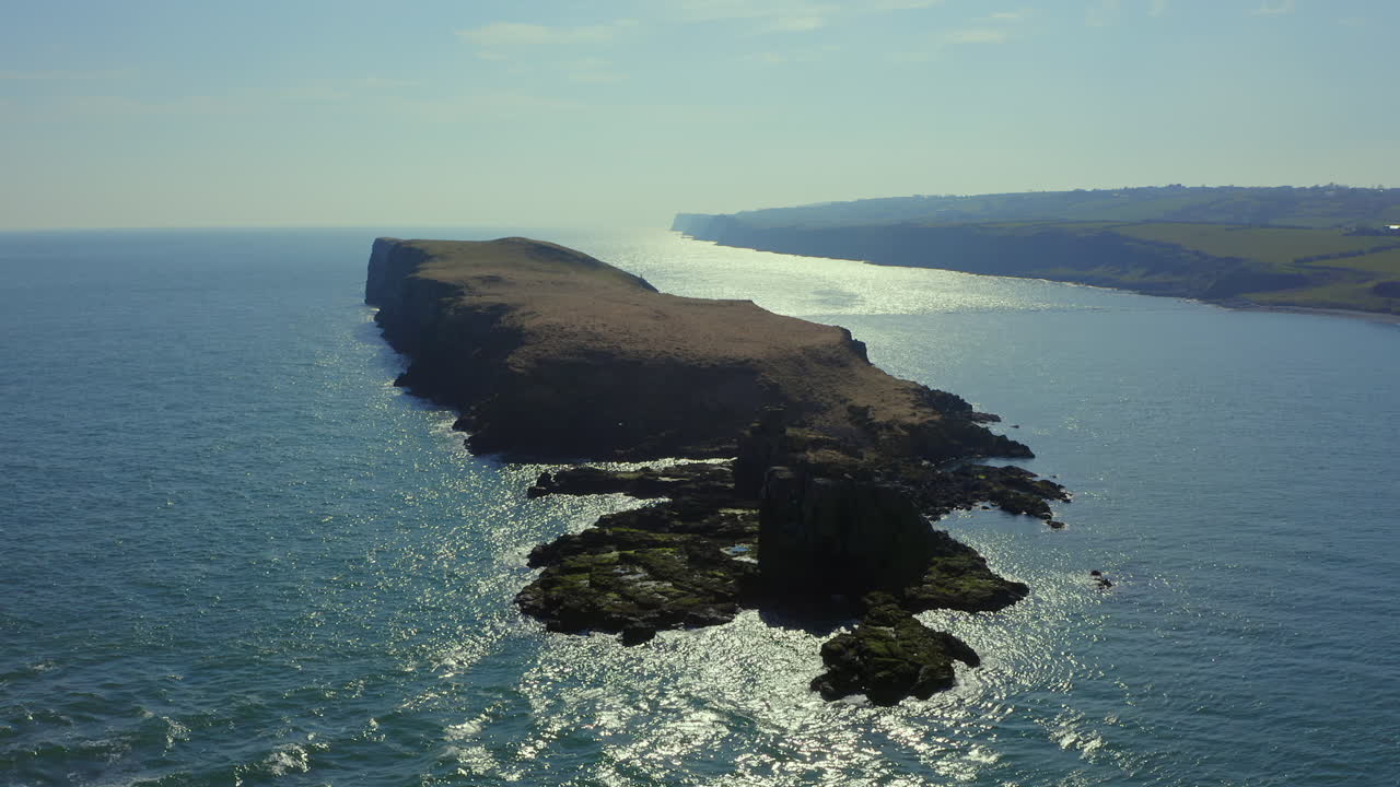 Backlit static aerial of Portmuck Island, Antrim, with magical slow-motion sea ripples.