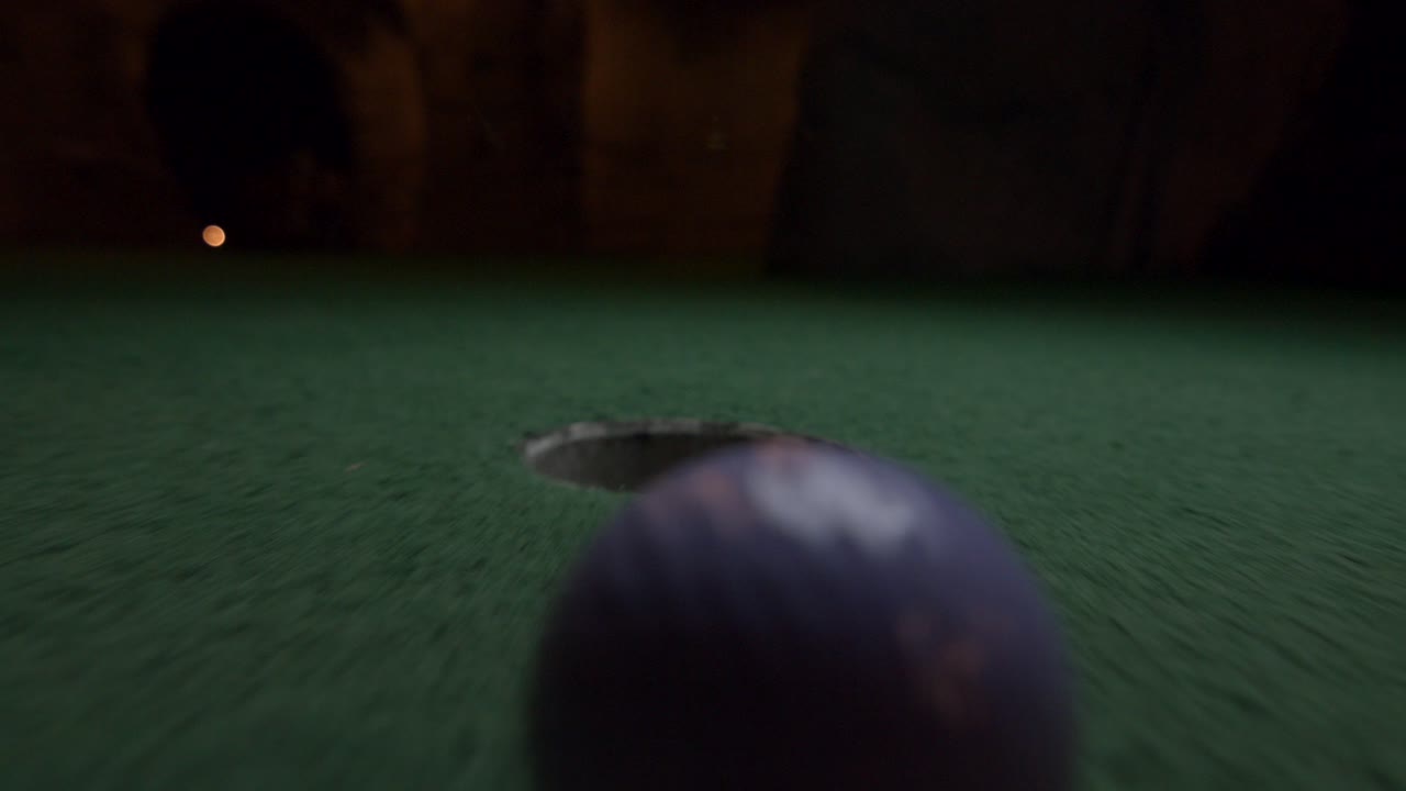 Una pallina da minigolf viola cade nella buca e rimbalza nel raccoglitore su un campo da gioco.