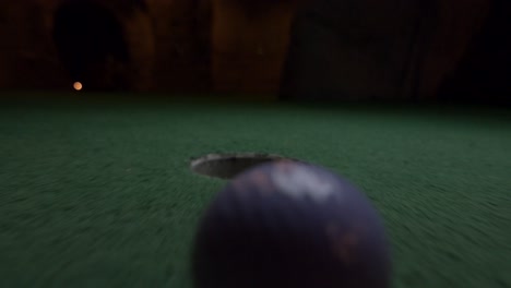 A-purple-mini-golf-ball-falls-into-the-golf-hole-and-bounces-in-the-pocket-on-a-course