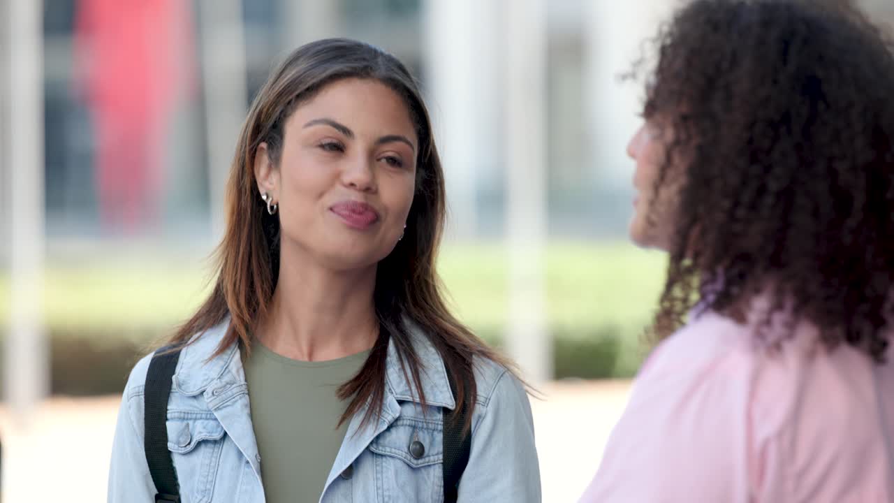 Donne afroamericane si notano e si salutano in piazza, una donna con giacca di jeans cammina con uno zaino.