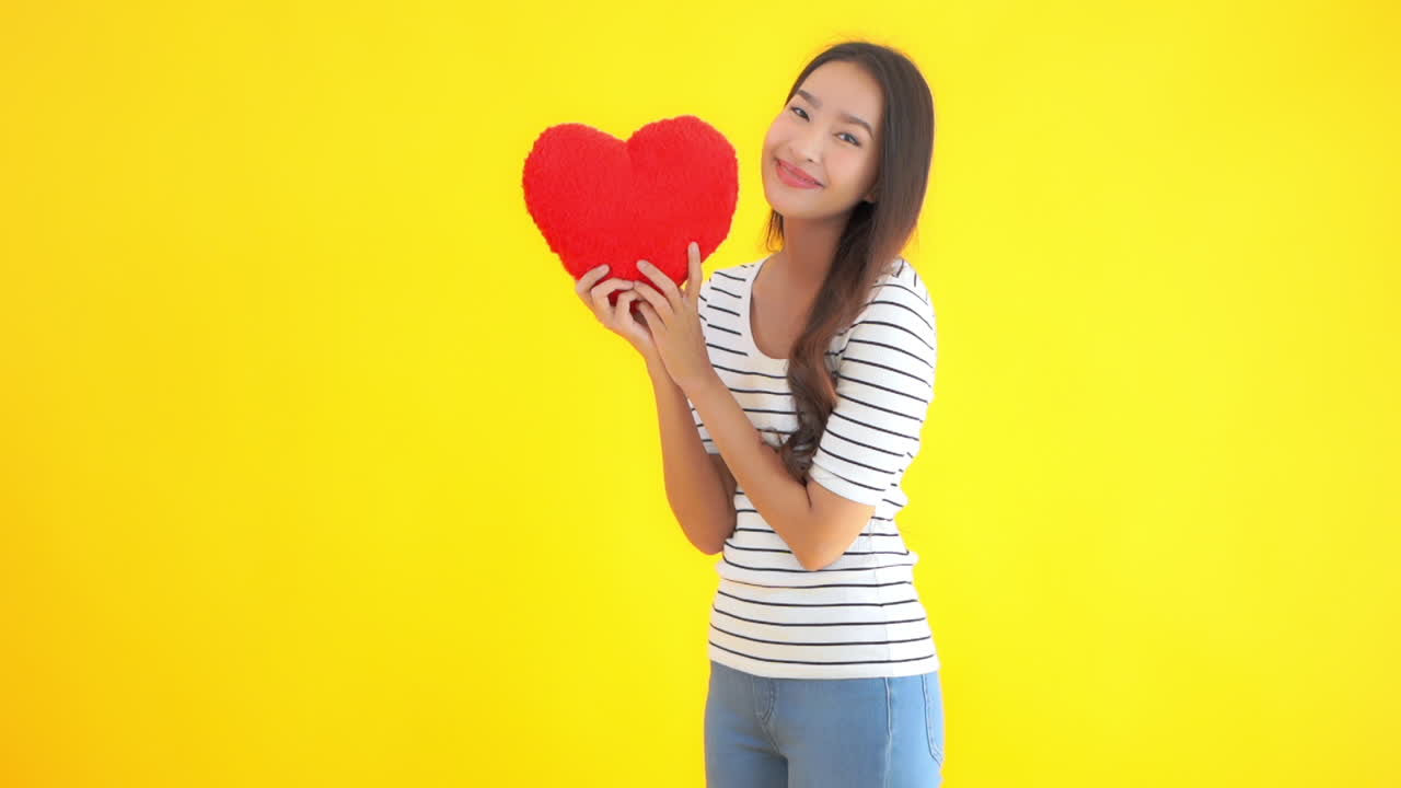 An attractive young Asian woman holds up a large red heart and smiles. Copy space