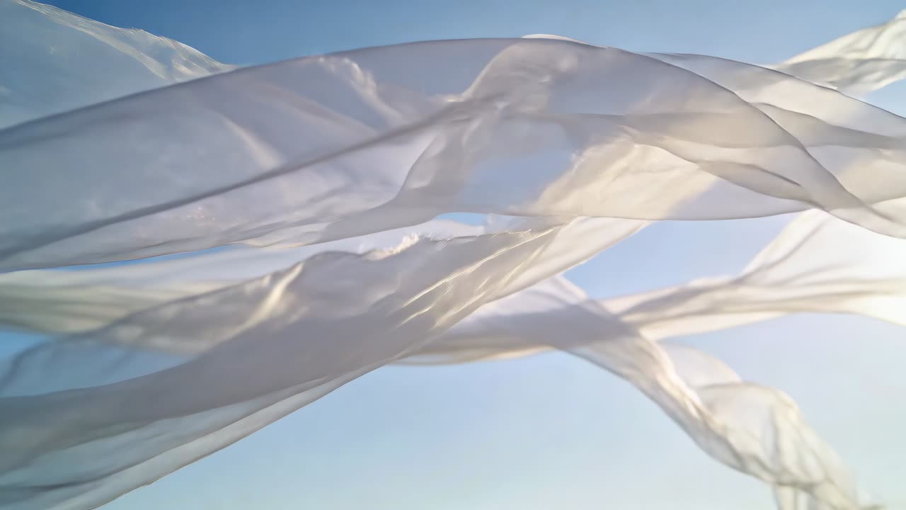 Draps de tissu blanc translucides flottant et ondulant dans un ciel bleu clair par une brise, avec la lumière du soleil.