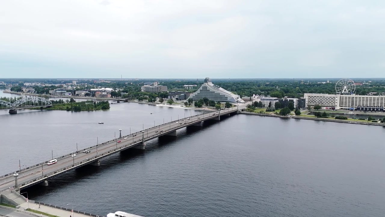 La Biblioteca Nazionale Lettone e il Ponte di Pietra attraversano il fiume Daugava mentre un drone scivola su acque calme verso la città.