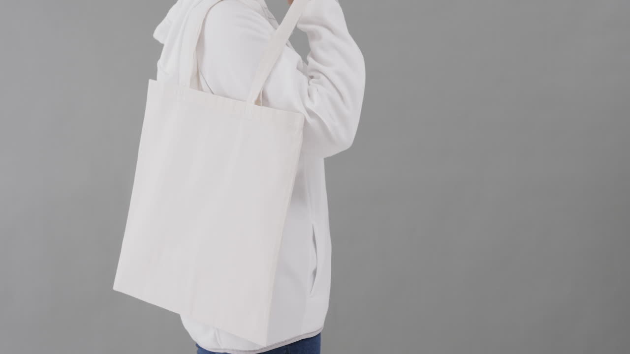 mujer caucásica con capucha blanca sosteniendo una bolsa blanca sobre un fondo gris, espacio de copia, cámara lenta