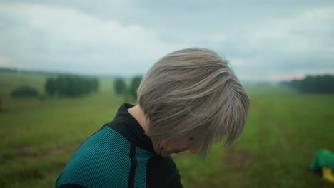 검은색과 초록색 의상을 입은 여성의 측면 뷰, 눈이 닫혀, 조용하고 조용한 야외 환경에서 그녀의 머리를 오른쪽에서 왼쪽으로 부드럽게 기울이고, 그녀는 긴장을 풀기 위해 주의 깊은 목 스트레칭을 연습합니다.