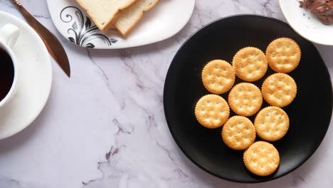 person picking up crackers from a plate of crackers, tea and bread on marble table