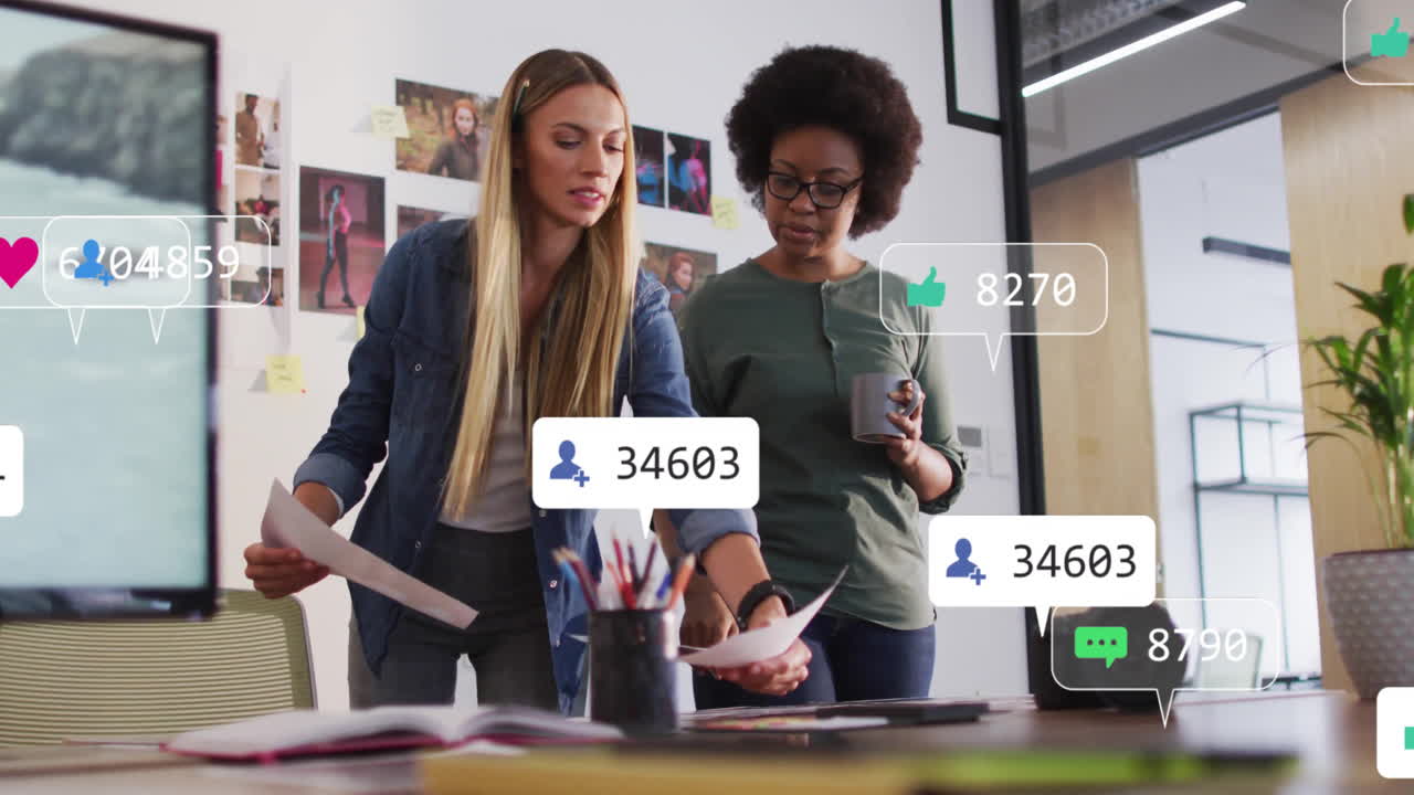 Animation of media icons over diverse female colleagues discussing work in office