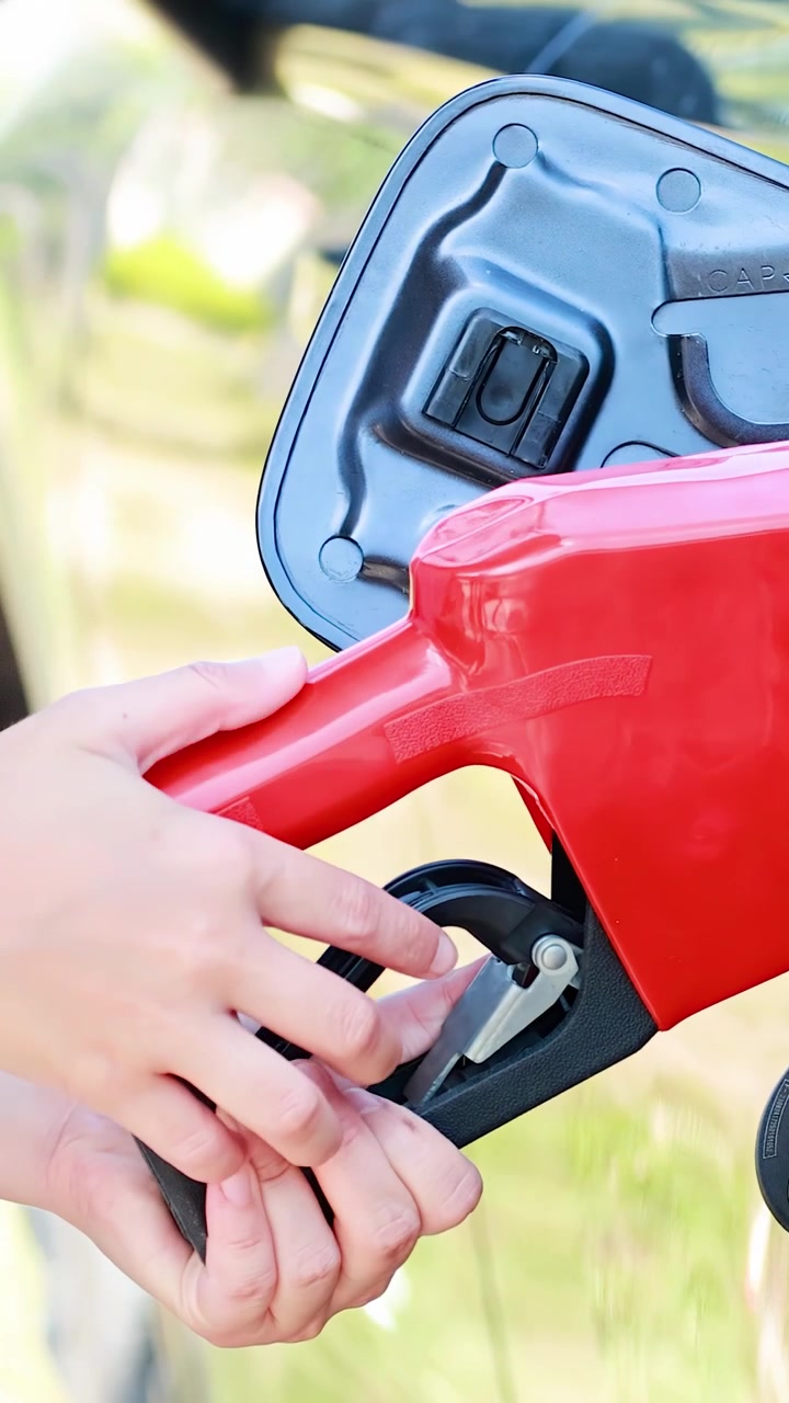 Mano inserta boquilla de combustible roja en el tanque del coche, luz diurna brillante, primer plano, gasolinera al aire libre