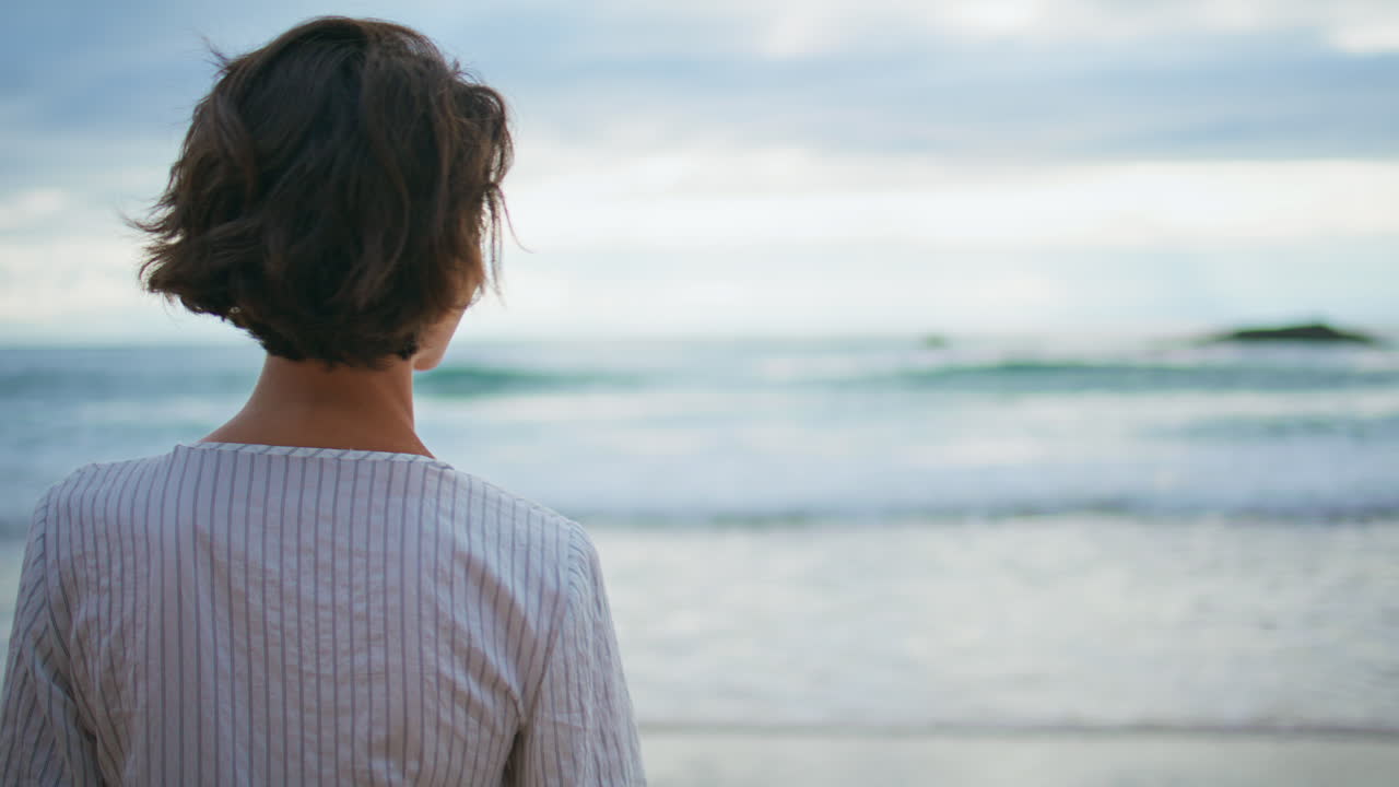 매력적인 여성이 바다를 바라보고 있다. 미소 짓는 소녀가 해변에서 휴식을 취하고 있다.