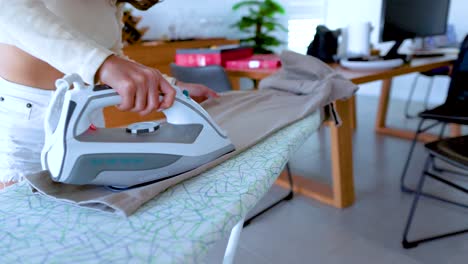 a person irons pants on a board in a bright, modern room, emphasizing daily chores and domestic life
