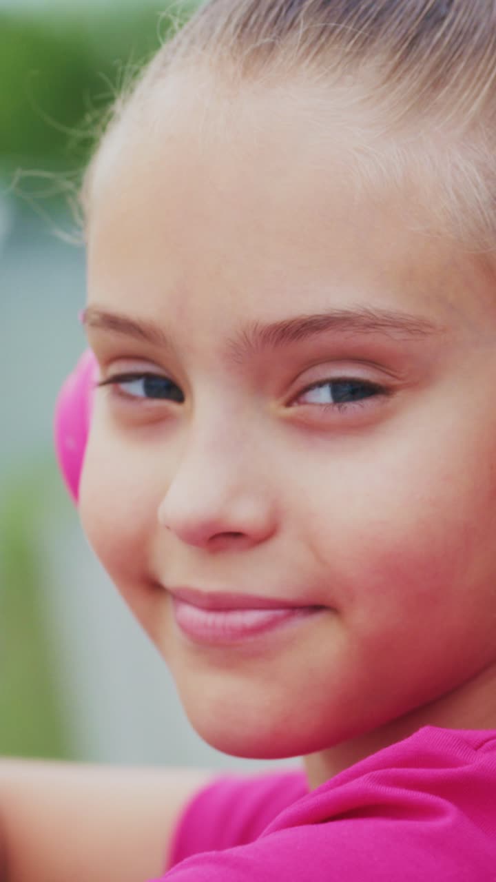 A confident young girl in pink attire displays a charming smile, showcasing her joy and self-assurance in this captivating moment captured on video