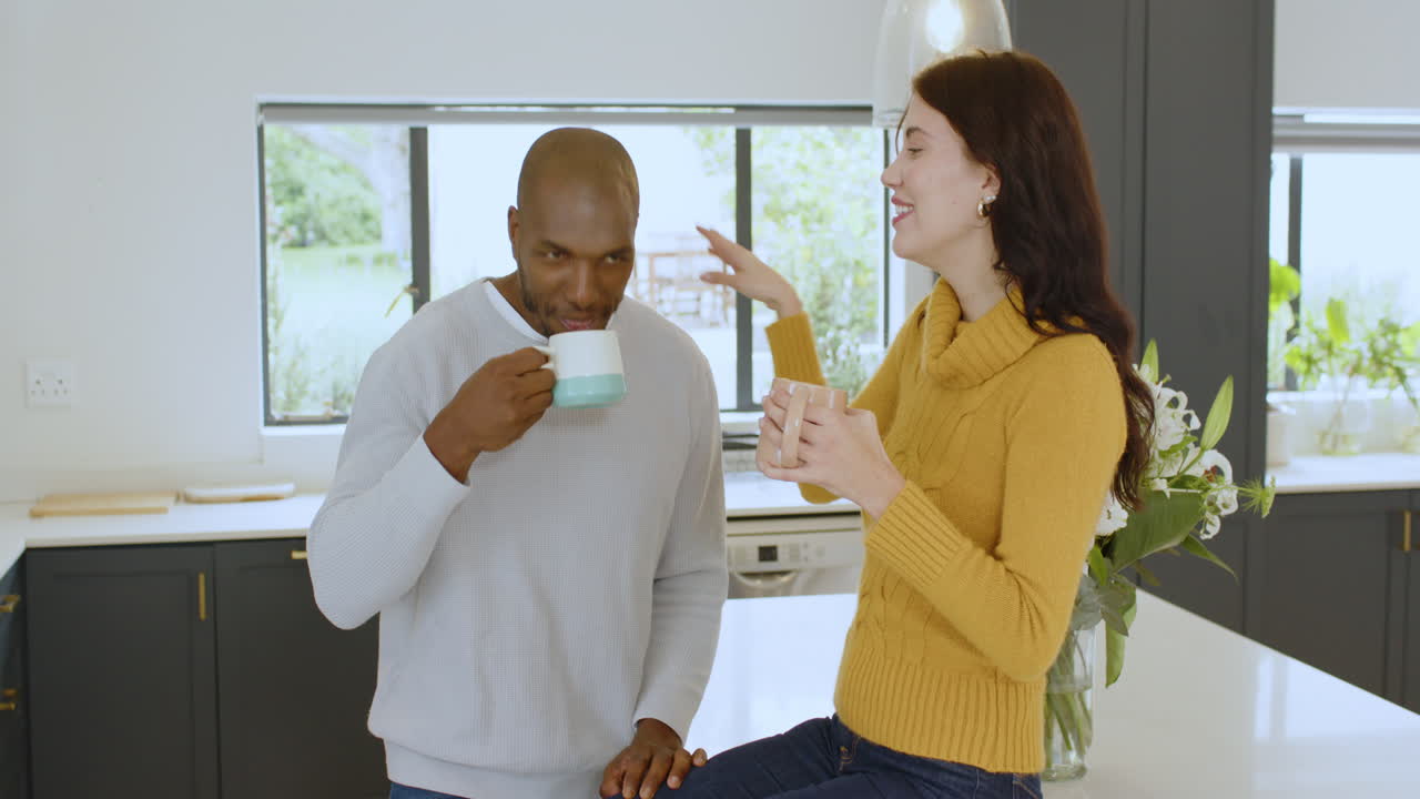 Multiracial couple enjoying coffee together in modern kitchen, sharing warm conversation, at home