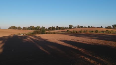 along the plowed empty field, view of the blue sky, long shadows and trees