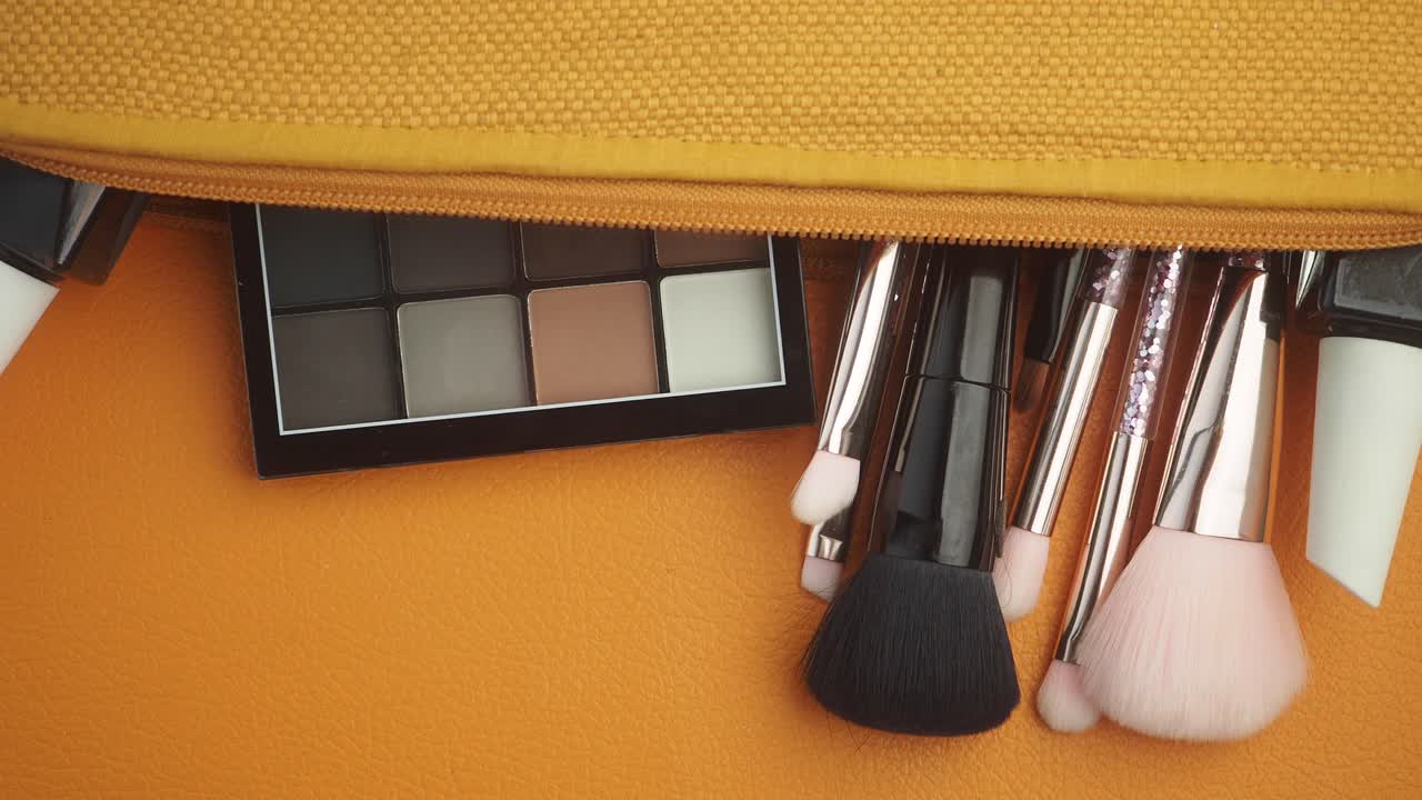 Makeup essentials spilling from a cosmetic pouch on an orange surface
