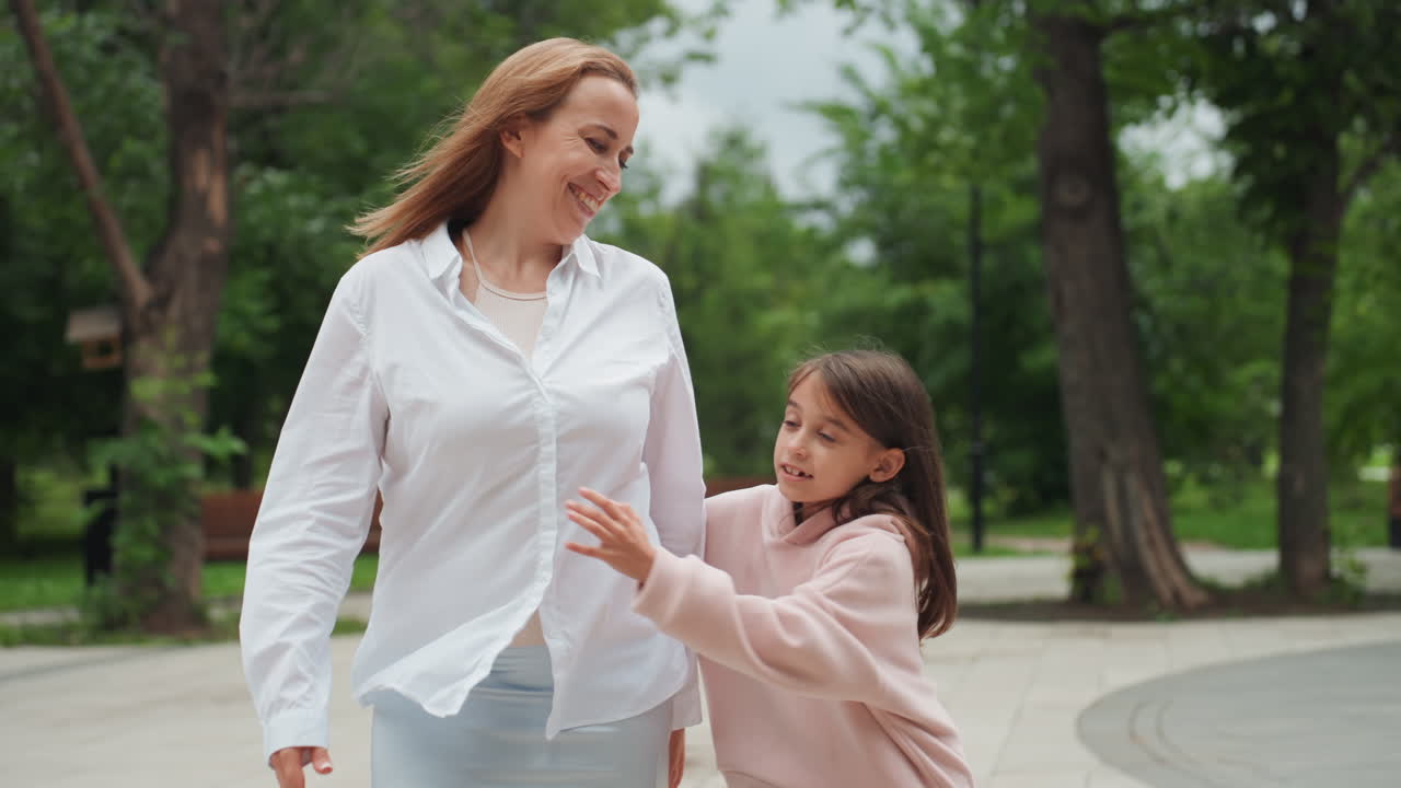 Mamma che cammina con la figlia nel parco tenendosi per mano, sguardo protettivo e sorriso gentile mentre passeggiano tra alberi e panchine con vestiti casual e luce soffusa del pomeriggio, momento di vita spontaneo