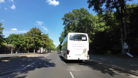 viewed from a car. the road is lined with lush, green trees under a vibrant blue sky. a bus and a few cars are visible, contributing to the bustling urban atmosphere of the city