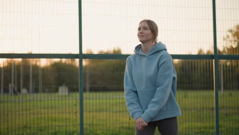 young female volleyball player in focus playing with blurred background showing open field and other sports facilities, demonstrating athletic skill and practice in outdoor environment