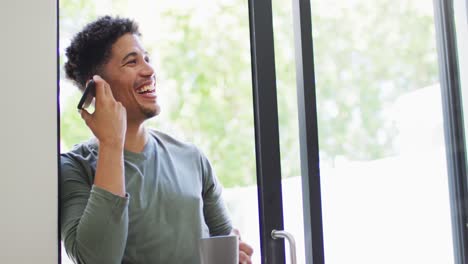 Happy-biracial-man-talking-on-smartphone-and-drinking-coffee