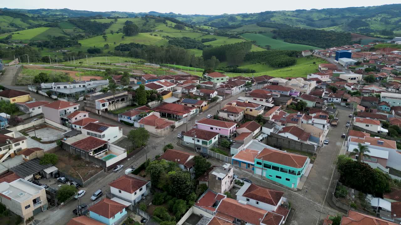 aerial view going down of a small neighborhood with orange roofs houses and lined streets surrounded by green hills - Bueno Brandao, Minas Gerais, Brazil
