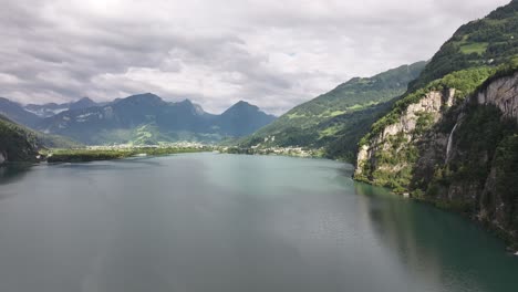 scenic aerial view of walensee lake in switzerland, with towering cliffs, cascading waterfall, and lush alpine mountains under dramatic clouds