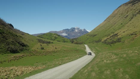 car driving on gravel road in grass valley towards moke lake, new zealand