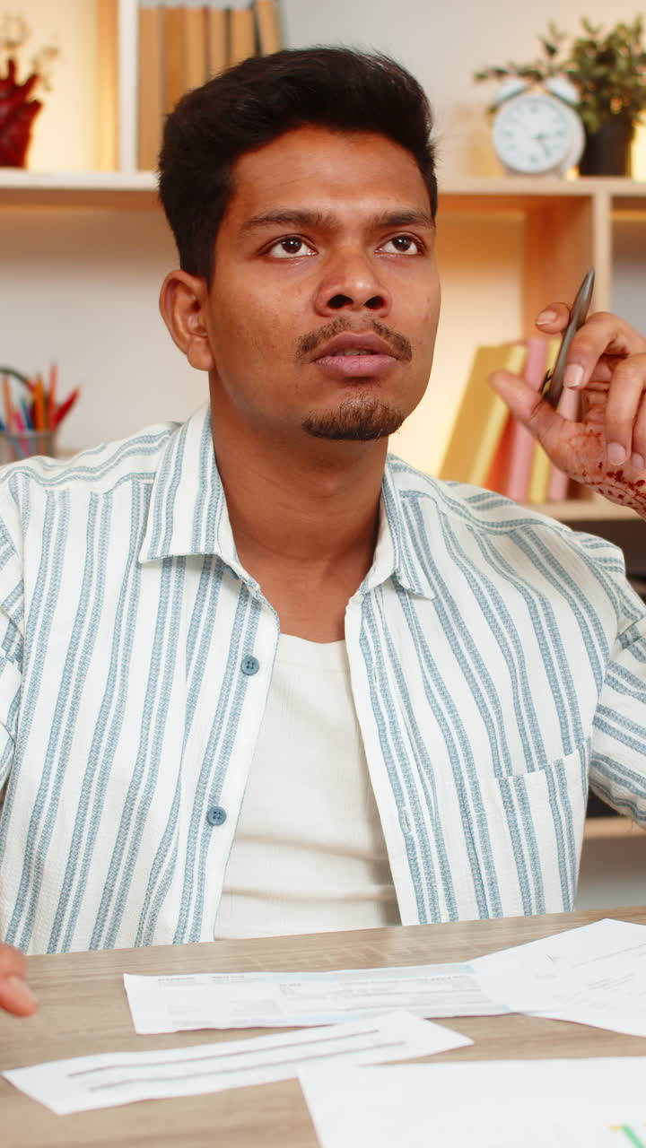 Indian man on home table thinking with pen near lips while making serious decision during work shift