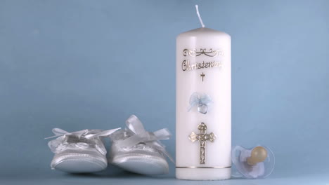 baby shoes falling beside baptism candle on blue background