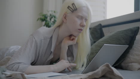 young woman studying on bed with laptop