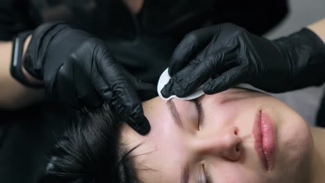 make-up artist wipes the client's eyebrows with a cotton pad after the procedure