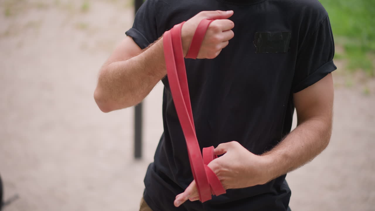 Resistance Wrap In Park Setting, Man Performing Steady Arm Exercises With Visible Tattoo In Park Environment, Consistent Resistance Band Workout Focused On Forearm Muscles In Peaceful Park Setting