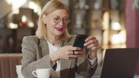 Cheerful-Senior-Businesswoman-Using-Smartphone-in-Cafe