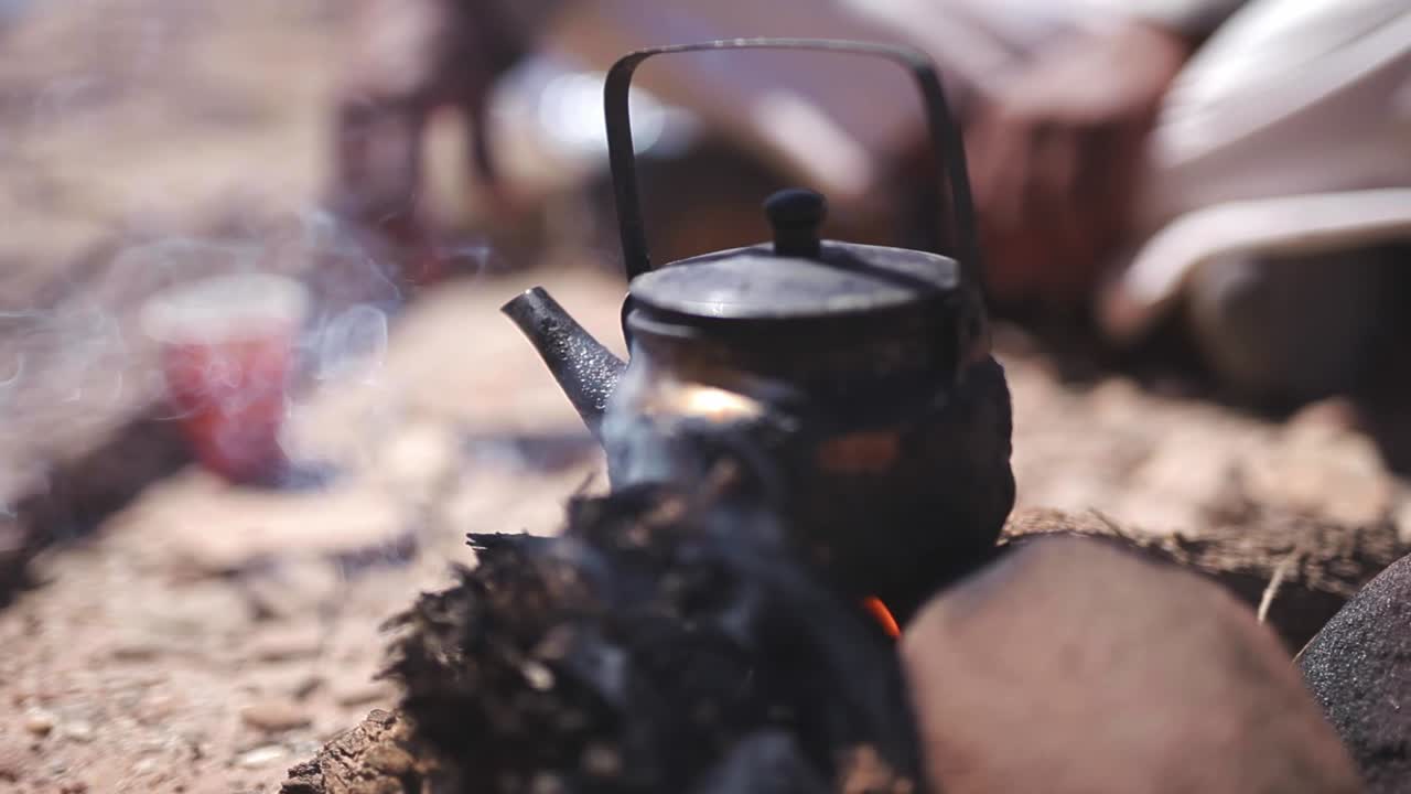Teapot in hot coal, blurry bedouin at the background, arid desert, Wadi Rum, Jordan, static shot