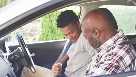 happy african american father and adult son putting on seatbelts in car before driving, slow motion