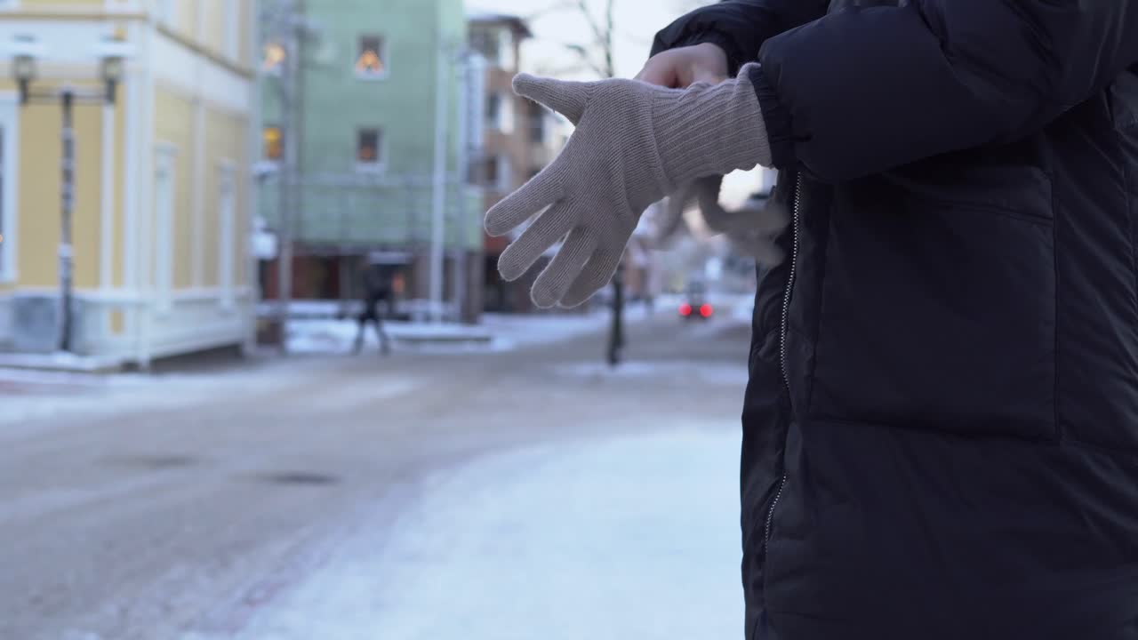 A young woman puts on warm gloves on a snowy street during a cold winter day