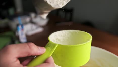 close up of pouring flour into light green plastic measuring cup