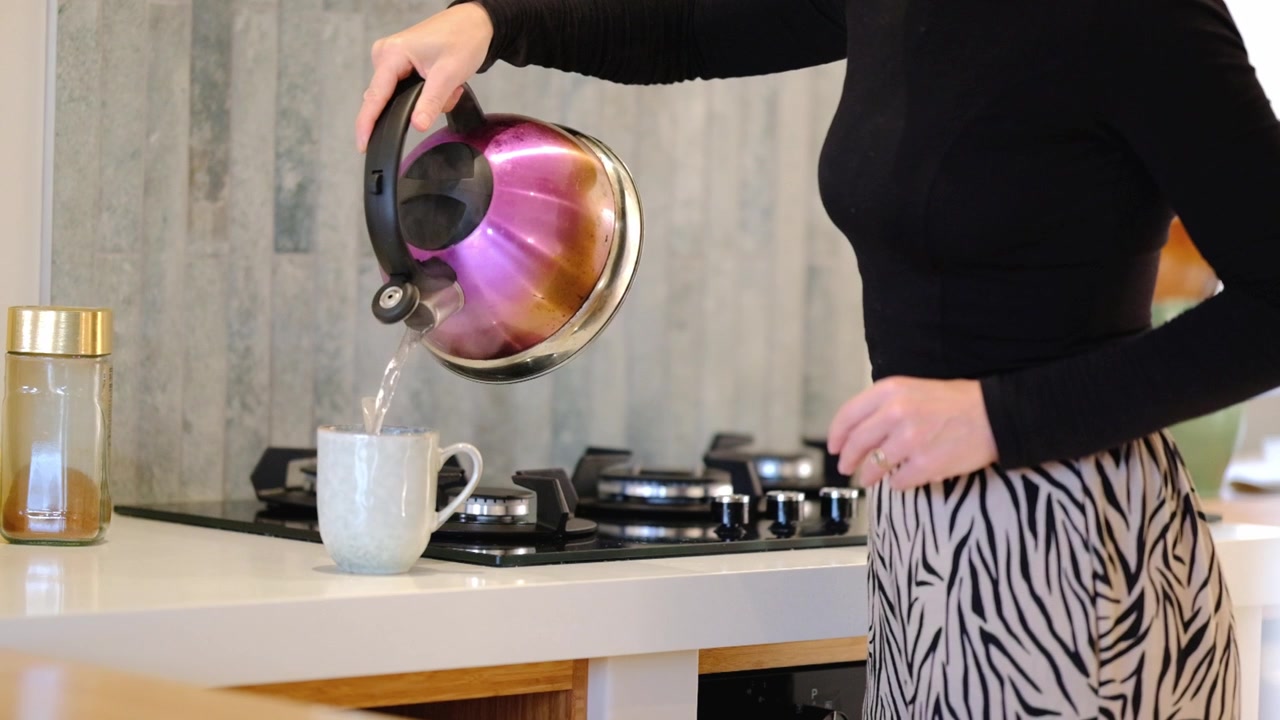 Una donna mette caffè istantaneo in una tazza e versa acqua bollente da un bollitore.