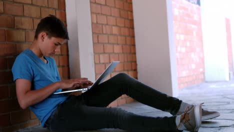 schoolboy sitting in corridor and using laptop