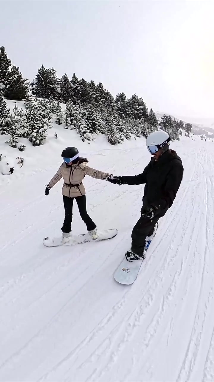 Coppia che fa snowboard insieme su un pendio montano innevato