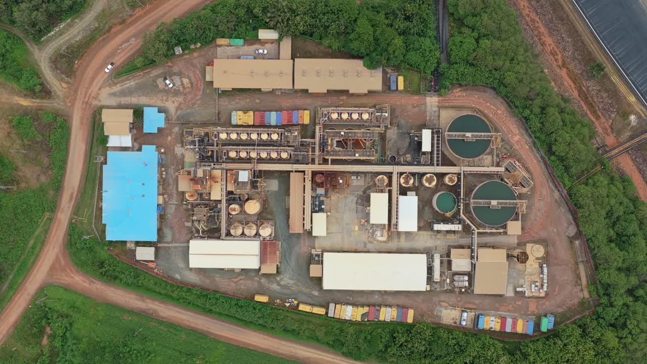 High aerial view showing an industrial mining operation with processing facilities, tanks, and buildings surrounded by lush green jungle vegetation