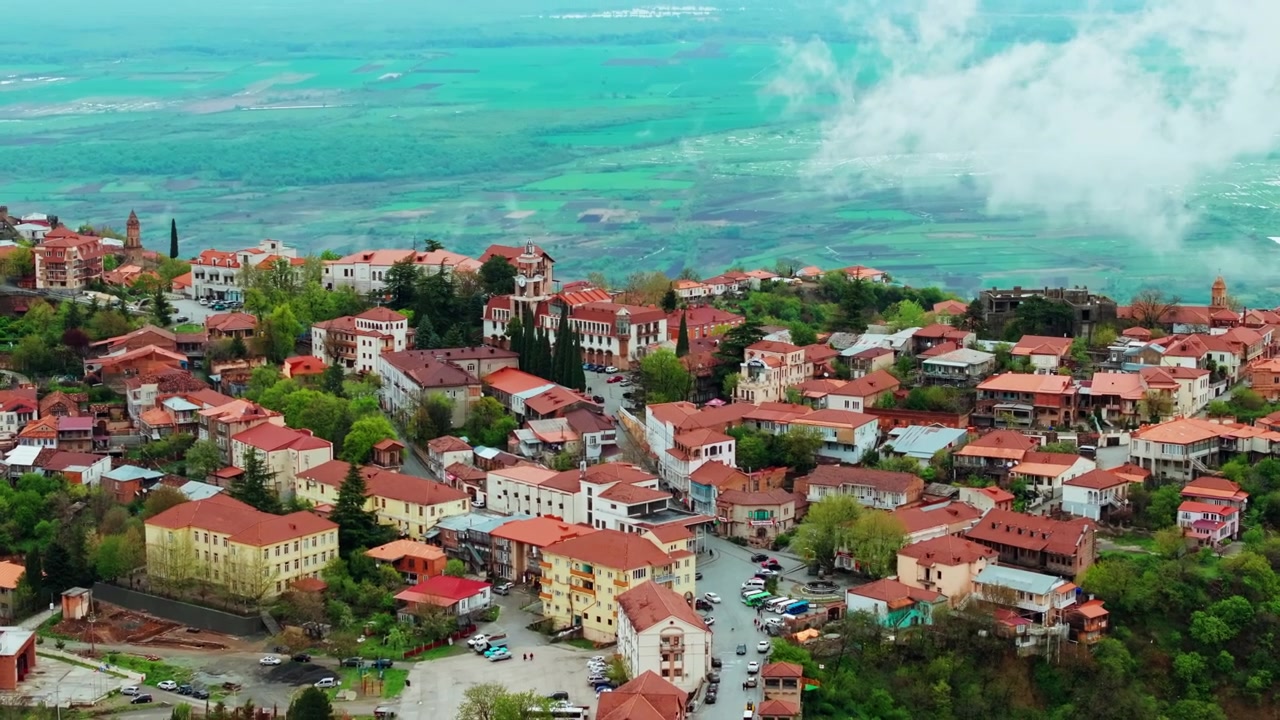 Gürcistan'ın Sighnaghi şehrinin geniş bir havadan görünümü; tepe üzerindeki sokakları, kale surlarını ve çevresindeki doğal güzelliği vurguluyor.