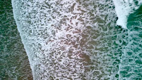 static overhead shot of the sea as it crashes into the beach