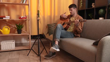 man playing acoustic guitar on a couch at home