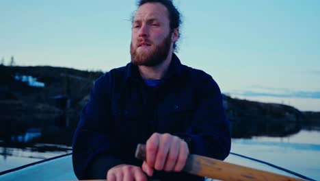 a caucasian man with a beard is rowing a boat over a lake. close-up shot