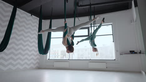 entrenador y mujer joven practicando gimnasia aero con suspensiones en el gimnasio. grupo de dos jóvenes mujeres hermosas yogi haciendo práctica de yoga aéreo en hamacas verdes en el club de fitness