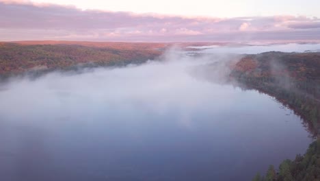 aerial sunrise wide shot flying through cloud fog to reveal misty lakes and pink clouds and fall forest colors in kawarthas ontario canada