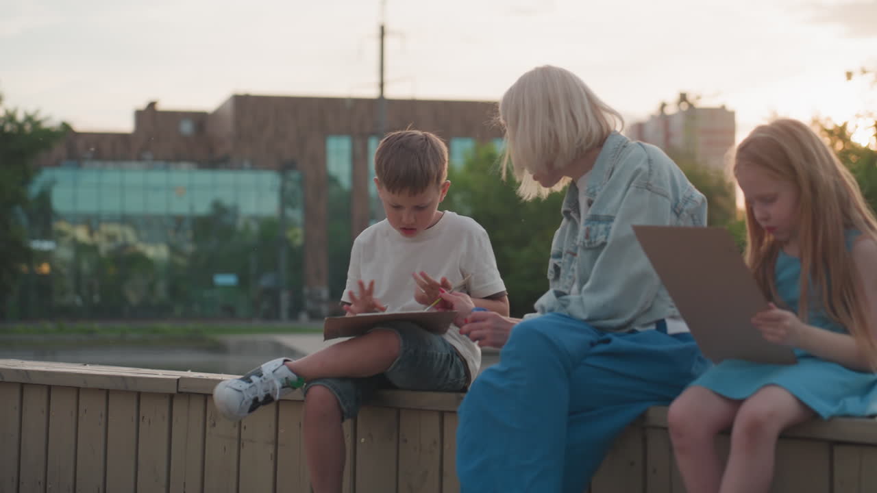 modern fair skinned mother guiding teenage boy in painting with brush by pool under soft sunset sky, mother demonstrating strokes from palette jar while boy focuses on board, warm evening reflection